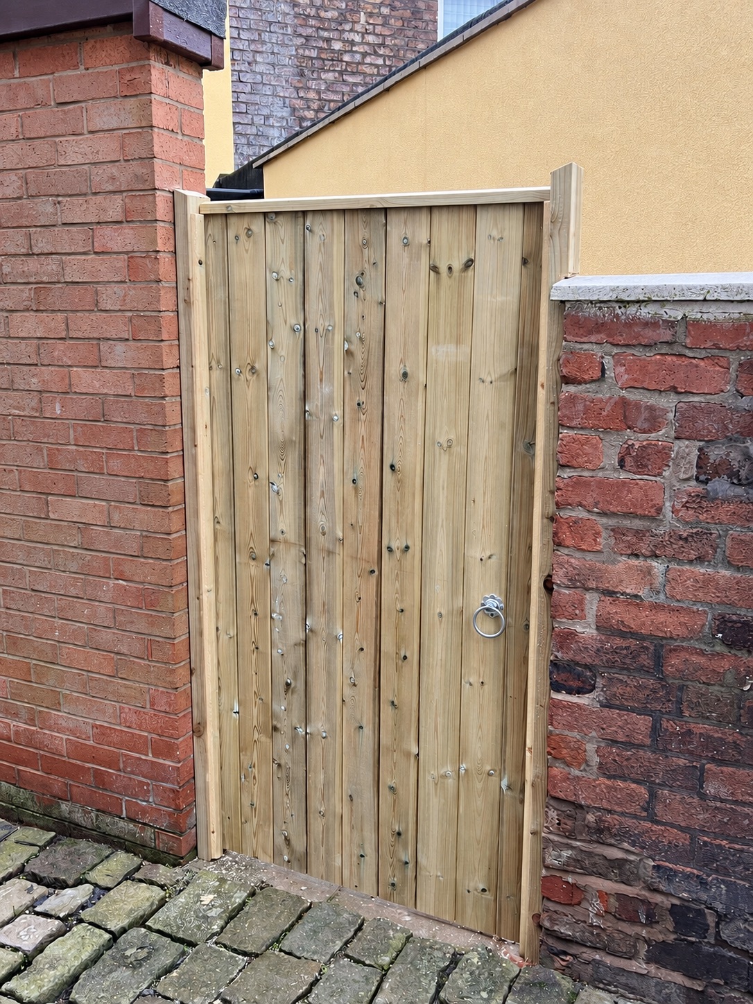 Tall natural timber gate fitted between brick walls
