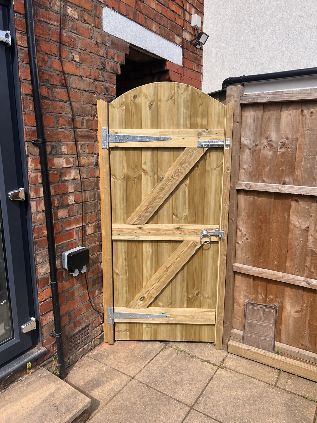 Arched-top ledge and brace timber gate beside a brick house